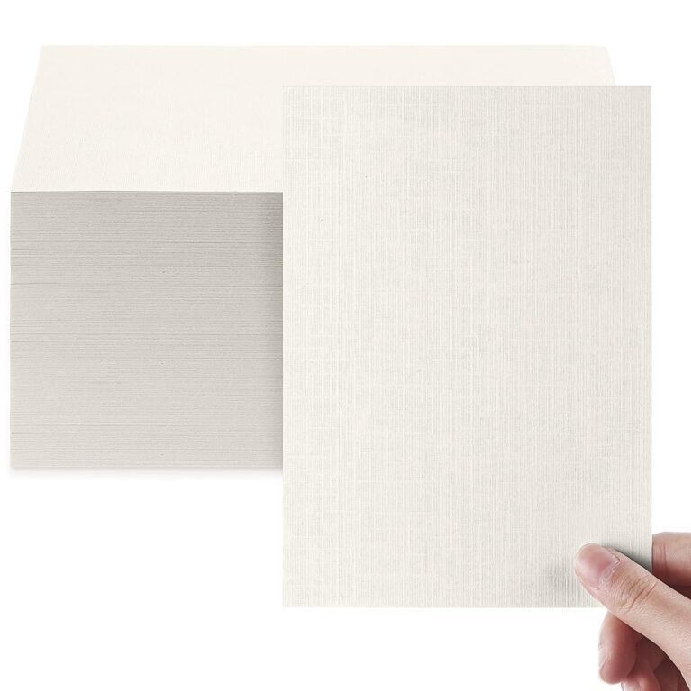 A hand holds a textured sheet of light-colored paper beside a stack