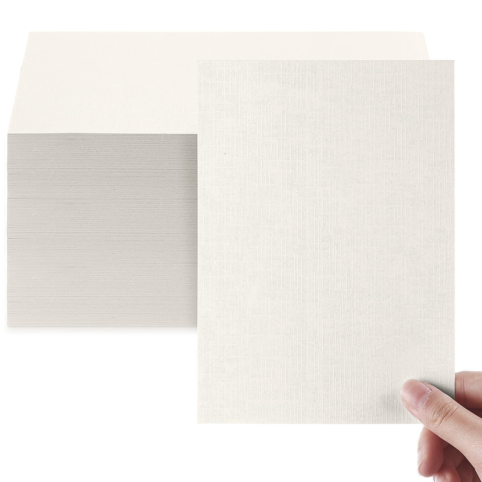 A hand holds a textured sheet of light-colored paper beside a stack